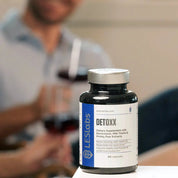 Natural hangover supplement bottle labeled 'DETOXX' by LES Labs on a table with a blurred person in the background.