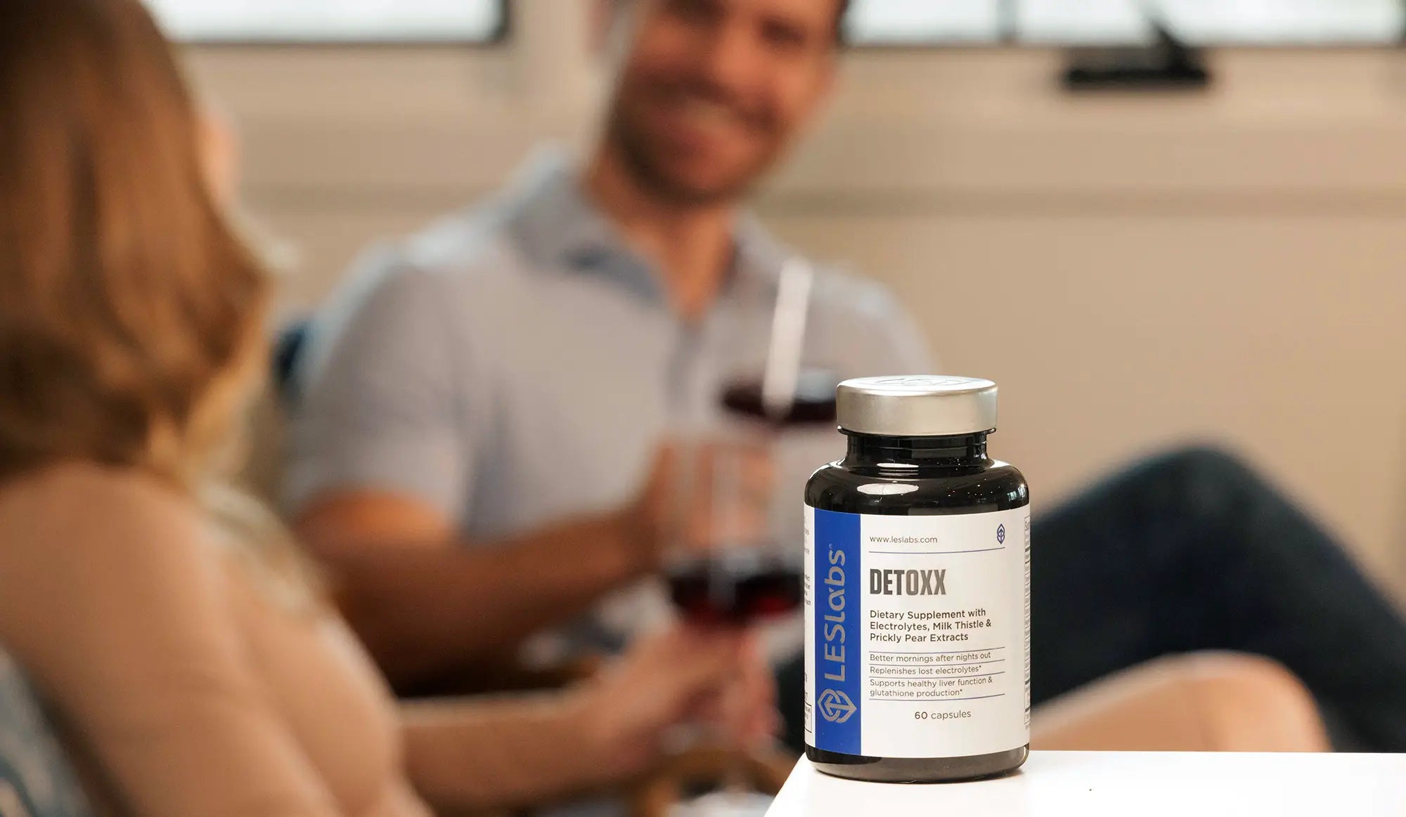 Bottle of Les Labs Detox supplement on a table with people in the background.