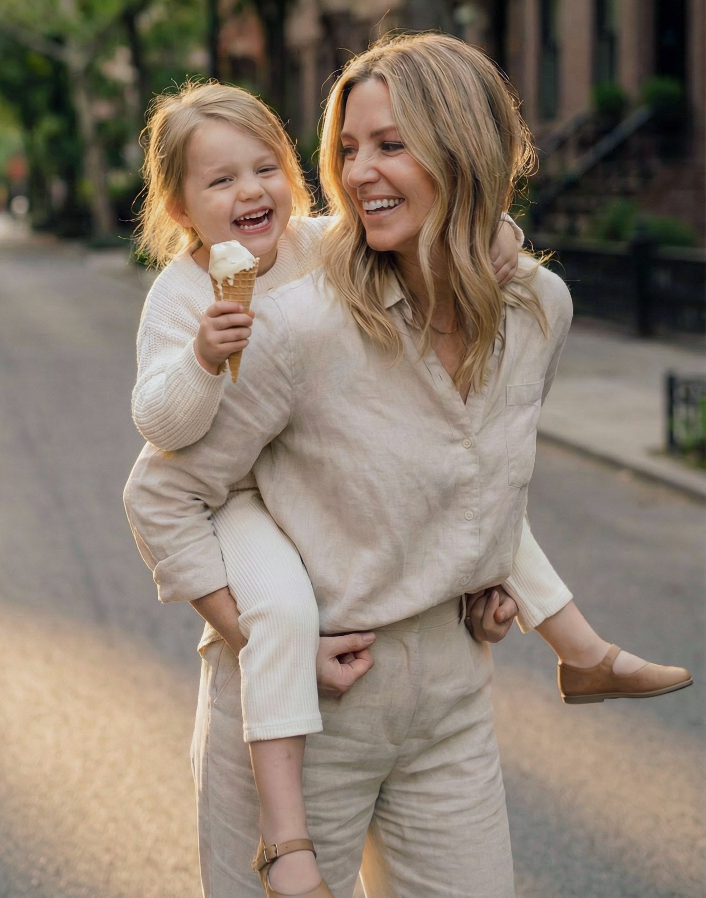 Happy, healthy woman holding a child who is eating an ice cream cone on a street.
