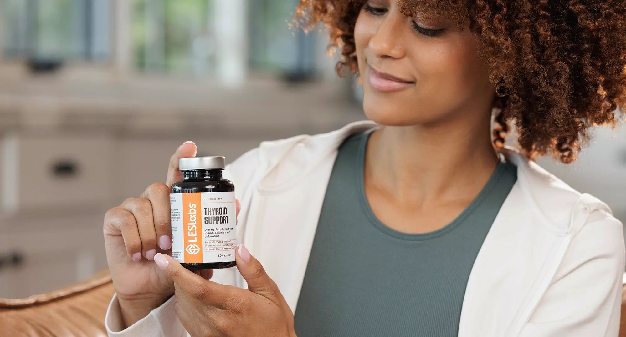 Woman holding a thyroid support supplement bottle in a casual setting